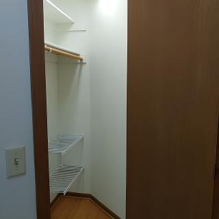 An empty closet with wooden shelves and an open wooden door.