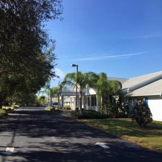 A sunny day with a road lined by palm trees and buildings.