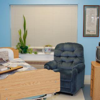 A cozy office space featuring a blue recliner chair, a desk cluttered with papers, and a green plant by the window.