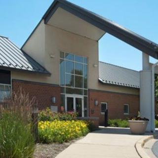 A modern building with a sloped roof and landscaped entrance under a clear blue sky.