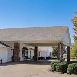 A welcoming entrance to a residential building surrounded by well-maintained landscaping under a clear blue sky.