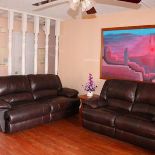 A cozy living room with dark leather sofas, vibrant artwork on the wall, and a wooden floor.