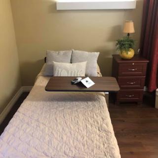 A cozy, minimalist bedroom featuring a single bed with decorative pillows and a nightstand.