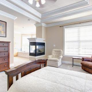 A spacious and bright bedroom featuring a cozy fireplace, comfortable seating, and natural light from the large window.