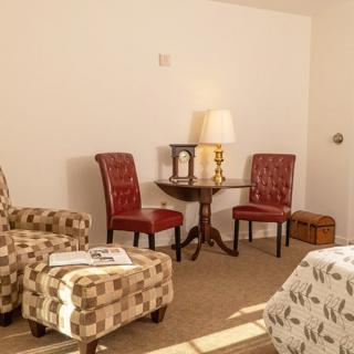 A cozy living room with a mix of patterned and solid-colored chairs, a small round table, and a warm lamp.