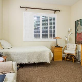 A cozy bedroom featuring a single bed, chair, and a painting on the wall.