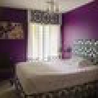 A modern bedroom with purple walls and a stylish chandelier.