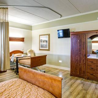 A clean and well-organized hospital room with a bed, television, and wooden furniture.