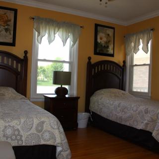 A cozy bedroom with two twin beds, adorned with floral bedspreads and curtains, featuring a wooden nightstand and framed artwork.