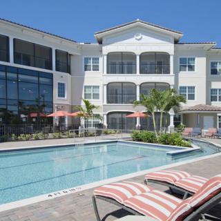 A sunny day at a modern apartment complex with a pool and palm trees.