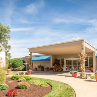 The image shows a building entrance with landscaped surroundings under a clear blue sky.