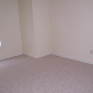 An empty room with carpeted flooring and plain walls.
