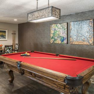 A stylish billiard room featuring a red-felt pool table and decorative wall art.