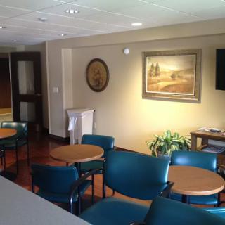 A quiet waiting room with several chairs and tables, decorated with a painting and a potted plant.