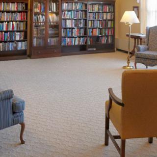 A cozy library setting with bookshelves, comfortable chairs, and a lamp.