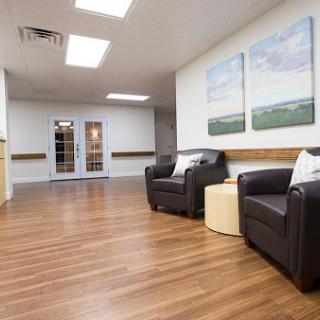 A spacious and modern waiting area featuring comfortable leather chairs, wooden flooring, and calming artwork.