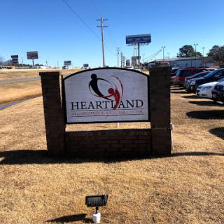 A sign for Heartland located in a well-lit outdoor area with visible parked cars.