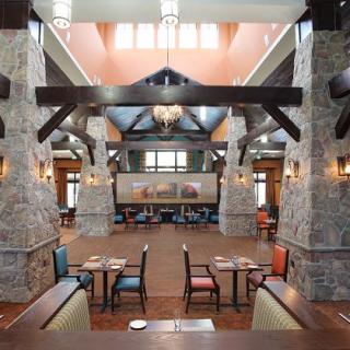 A spacious restaurant interior featuring stone pillars, wooden beams, and elegant chandeliers.
