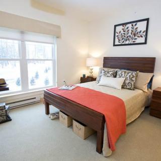 A modern bedroom with a neatly made bed, stylish decor, and natural light from a large window.