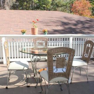 A sunny outdoor patio with a glass table and four chairs, decorated with potted plants in the background.