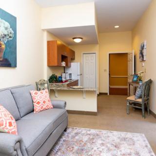 A cozy apartment living room with a couch, artwork, and a view into the kitchenette.