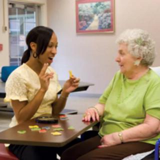 A caregiver and an elderly woman engaging in a conversation at a nursing home.