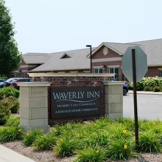Entrance sign for Waverly Inn with a building and landscaped area in the background.