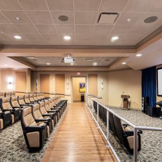 An empty auditorium with arranged seating and a projector screen at the front.