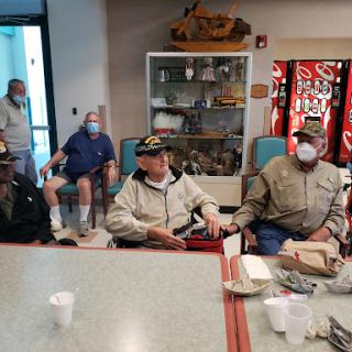 A group of individuals gathered indoors, some wearing masks, engaged in conversation.