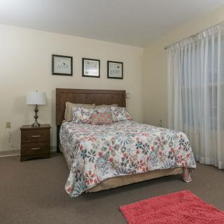 A cozy bedroom featuring a bed with floral bedding, a nightstand with a lamp, and framed art on the wall.