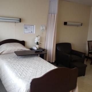 A hospital room with a bed, chair, and bedside table.