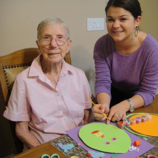An elderly woman and a caregiver engaging in a crafting activity together.