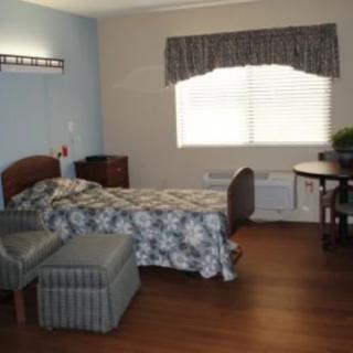 A cozy bedroom featuring a bed with floral bedding, an armchair, and a window with curtains.