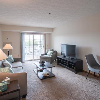 A cozy living room with modern furniture and a large television, featuring a sliding glass door that lets in natural light.