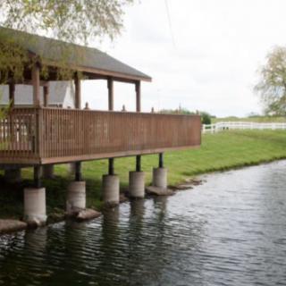 A wooden gazebo overlooks a serene lake surrounded by greenery.