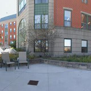 Outdoor view of an urban building with chairs and a tree.
