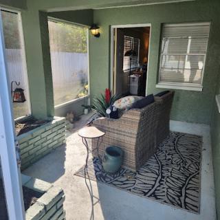 A cozy outdoor porch setup with comfortable seating and decorative plants, framed by green walls and natural light.