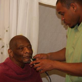 A caregiver providing grooming services to an elderly man.