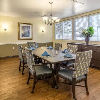 A beautifully set dining room with a large table and elegant chairs, featuring a chandelier and window views.