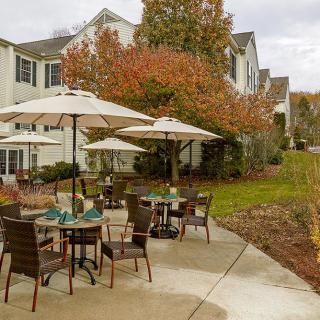 Outdoor patio with tables and chairs under umbrellas, surrounded by autumn foliage.