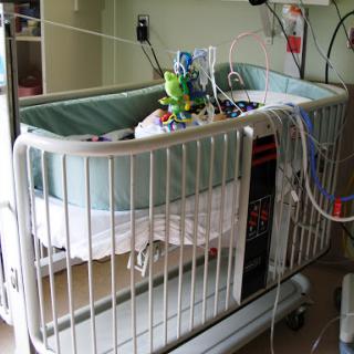 A crib in a hospital nursery, equipped with medical apparatus for an infant.