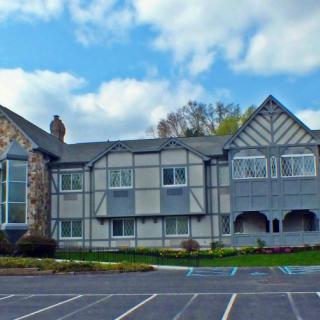 A Tudor-style building with a stone facade and gabled roof, set against a partly cloudy sky, is fronted by an empty parking lot.