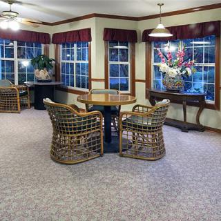 A cozy room with wicker chairs around a wooden table, featuring large windows and decorative plants.