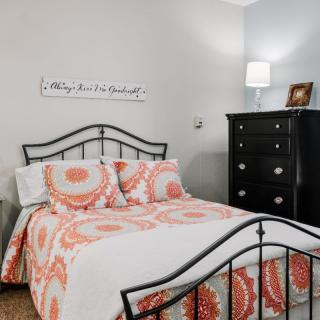 A cozy bedroom with patterned bedding and a black metal bedframe, accompanied by a dark wood dresser and a bedside lamp.