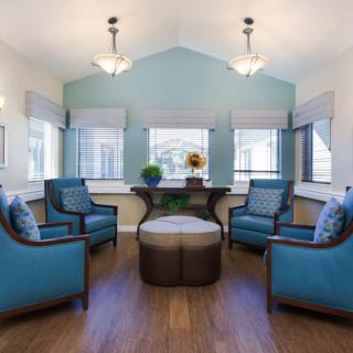 A cozy, well-lit living room with blue chairs and a central coffee table, featuring modern decor.