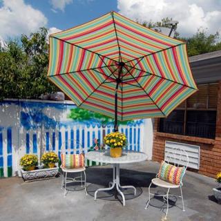 A cozy backyard patio with a colorful striped umbrella and a set of chairs around a table, adorned with potted flowers.