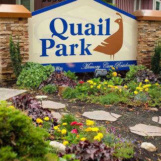 A landscaped garden with a 'Quail Park' sign surrounded by vibrant flowers.