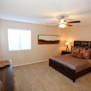 A cozy bedroom with a modern design, featuring a bed, nightstands, and a ceiling fan.