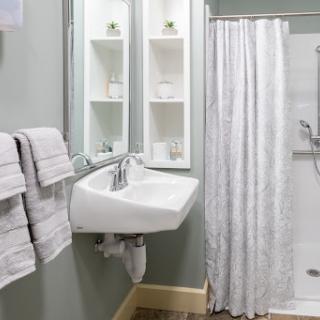 A modern bathroom featuring a sleek sink, a shower curtain, neatly arranged towels, and stylish storage.