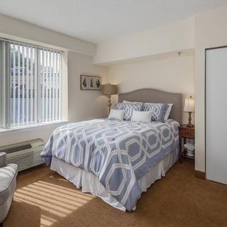 A cozy bedroom with a neatly made bed, soft lighting, and a large window.